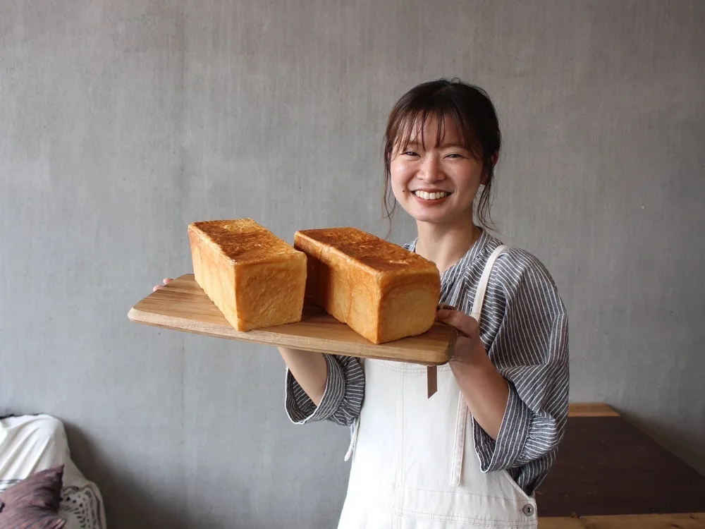 なーやんパン店主が焼きたての生食パンを掲げて微笑む様子